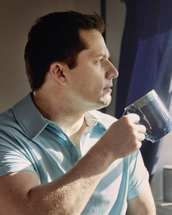 Un utente del sistema CGM Eversense tiene in mano una tazza blu mentre indossa il trasmettitore intelligente Eversense sul braccio